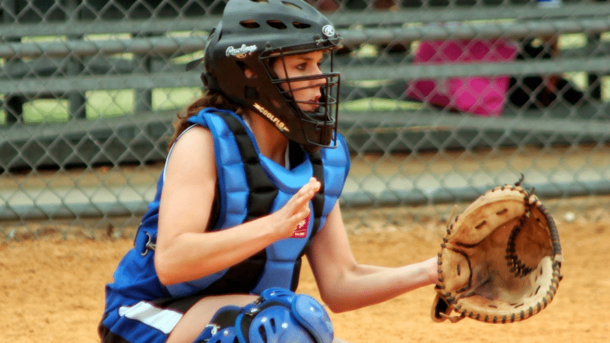 Softball catcher in blue ready to receive a pitch.