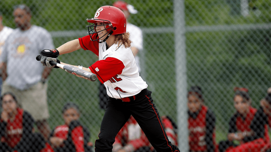 A softball batter holding a bat out and smiling