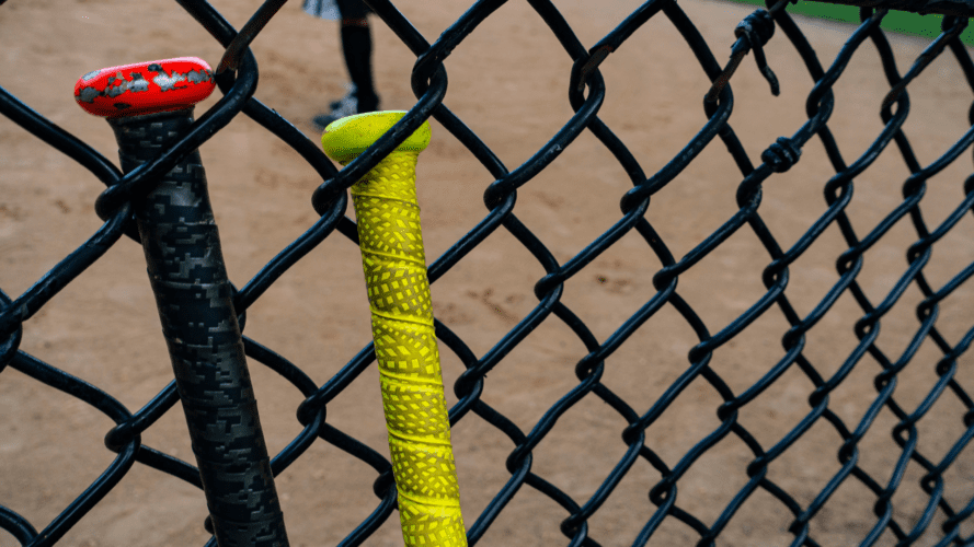 Softball bats leaning against a chain link fence