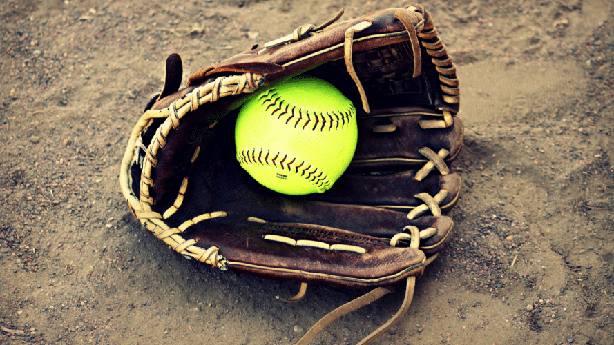 Brown glove on the dirt with vibrant yellow softball